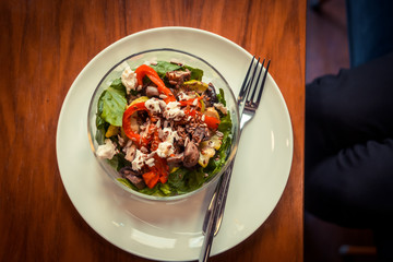 Glass bowl of healthy roasted vegetables salad on a wooden table. Low key food photography, warm toned filter