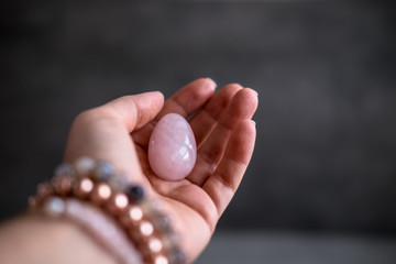 Woman holding in hand a vaginal (yoni) egg. Rose quartz crystal egg. Copy space