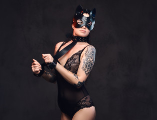 Sexy woman wearing black lingerie in BDSM cat leather mask and accessories posing on dark background. 