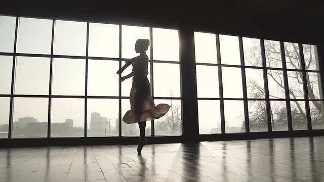 ballerina is spinning in a long fluttering dress. Ballet dancer in pointe shoes on the background of a solar window. slow motion