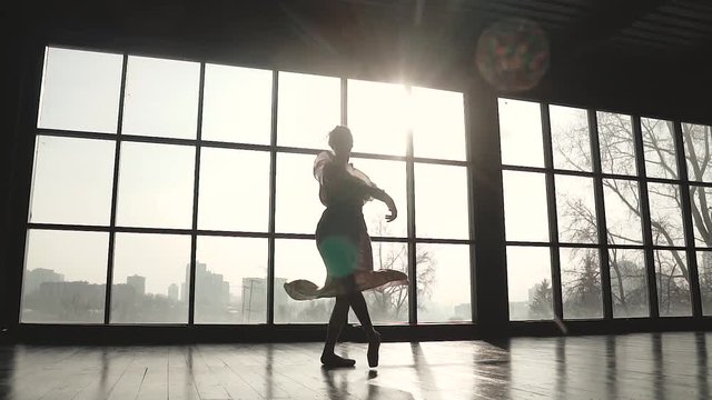 ballerina is spinning in a long fluttering dress. Ballet dancer in pointe shoes on the background of a solar window. slow motion