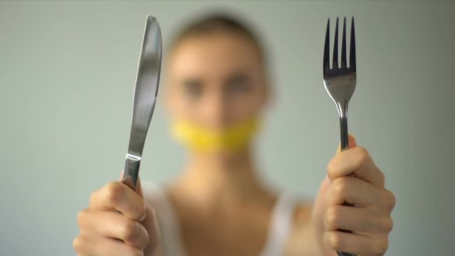 Girl closed mouth with tape-line, holding fork and spoon, diet, calorie counting
