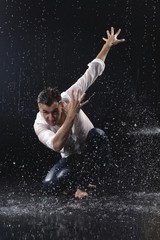 A young barefoot man wearing wet blue jeans and a white shirt expressively dances modern dances on...