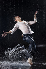 A young barefoot man wearing wet blue jeans and a white shirt expressively dances modern dances on...