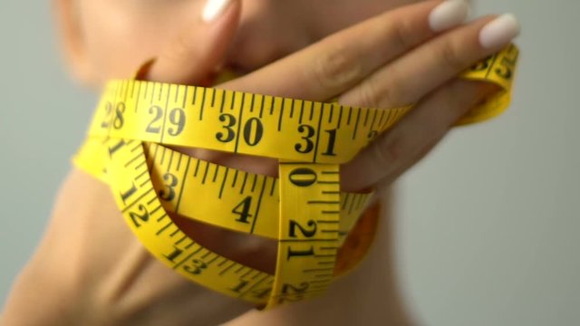 Closeup of girl closing mouth with measuring tape, bmi calculation, anorexia