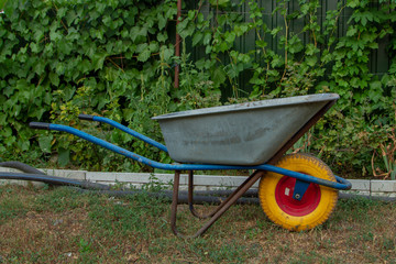 A metal wheelbarrow with a yellow wheel for home and garden. A wheelbarrow with blue handles and a...