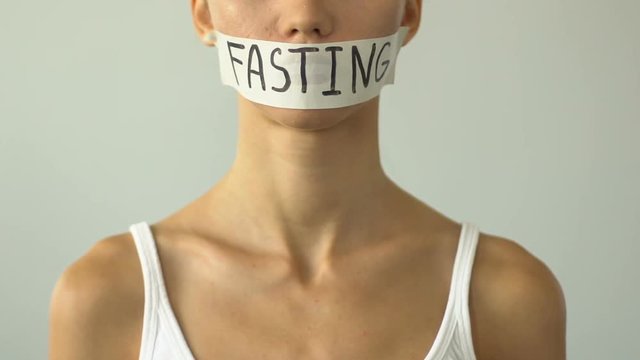 Fasting written on taped mouth of slim girl, concept of malnutrition, anorexia