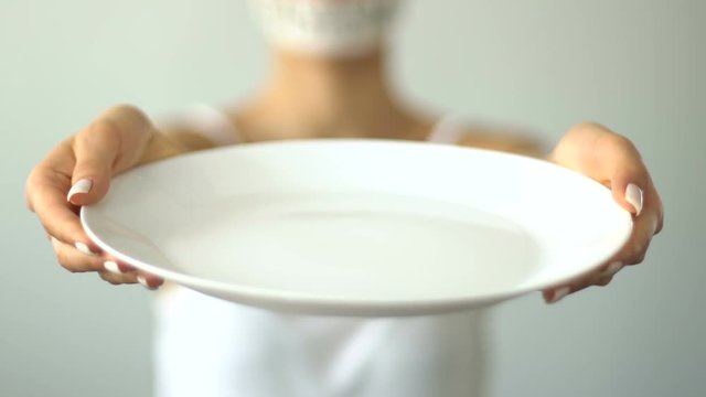 Fasting concept, girl with taped mouth holds empty plate, exhausted from hunger