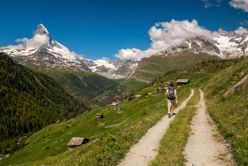 Female traveler with backpack hiking mountain trail and admiring views of Majestic Matterhorn...