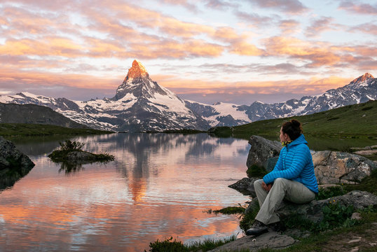 Morning shot of the golden Matterhorn (Monte Cervino, Mont Cervin) pyramid and  blue Stellisee lake. Female tourist enjoying view of early morning Matterhorn mountain is Valais Alps, Switzerland.