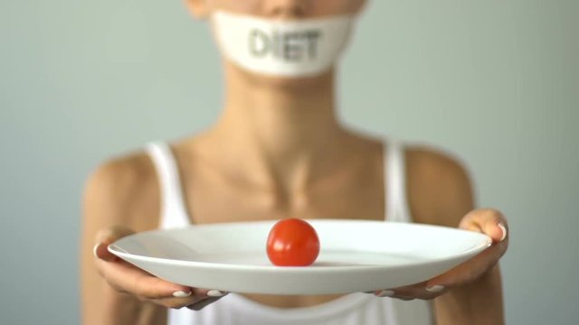 Anorexic girl with taped mouth holding small portion of food, diet restrictions