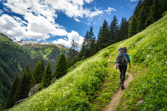 Female traveler with backpack hiking mountain trail and admiring views of Swiss Alps in Val de Bagnes area, Switzerland.
