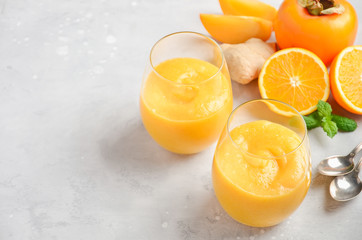 Fresh healthy smoothie with persimmon, orange and ginger on gray concrete background.