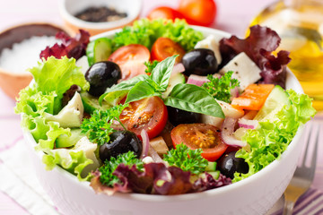 Fresh Greek salad with vegetables, feta cheese and black olives in white bowl on purple wooden background