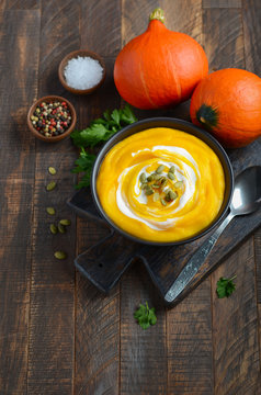 Pumpkin cream soup with cream and pumpkin seeds on rustic wooden table.