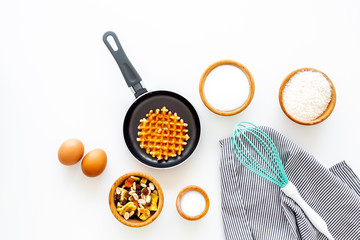 Preparing belgian waffles. Waffle on pan near whisk for whipping and ingrdients. Eggs, flour, sugar, dried fruits on white background top view space for text
