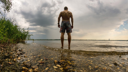 Trainierter Mann geht in einen See zum Schwimmen bei heranziehendem Unwetter