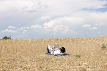 Obraz premium Chico joven leyendo un libro en el campo con nubes