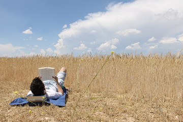 Chico joven leyendo un libro en el campo con nubes