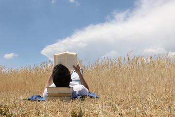 Chico joven leyendo un libro en el campo con nubes