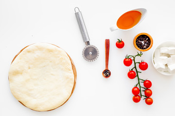 Make pizza concept. Pizza dough and ingredients for filling. Cherry tomatoes, olive oil, cheese mozzarella, spices near knife for pizza on white background top view mockup space for text