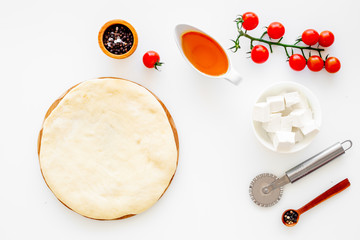 Make pizza concept. Pizza dough and ingredients for filling. Cherry tomatoes, olive oil, cheese mozzarella, spices near knife for pizza on white background top view mockup