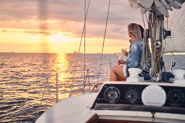 Female friends relaxing on the yacht with glasses of wine in the hands, during sunset on the high seas.