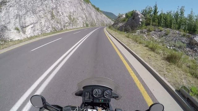 Motorcyclist Rides on a Beautiful Landscape Mountain Road in Austria. First-person view. POV. Mototravel. Viewpoint of a biker riding down a scenic and empty road toward the mountains.