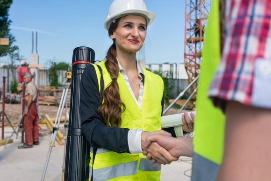 Low-angle view of a female architect and an engineer or supervisor smiling while shaking hands on the construction site of a new building
