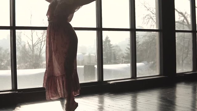 portrait of a young ballerina dancing on tiptoes in pointe shoes in a long fluttering dress on the background of the window. Silhouette of a ballet dancer. slow motion