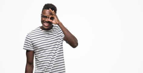 Fototapeta premium Young african american man wearing glasses and navy t-shirt doing ok gesture with hand smiling, eye looking through fingers with happy face.