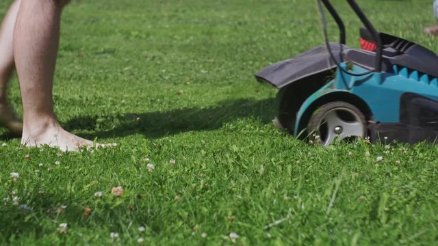man barefoot cuts grass lawn mower