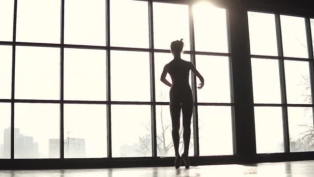 silhouette graceful ballerina on the background of a large window. Ballet dancer in pointe shoes. slow motion