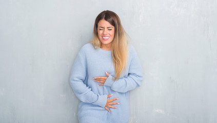 Young adult woman over grey grunge wall wearing winter outfit with hand on stomach because nausea, painful disease feeling unwell. Ache concept.