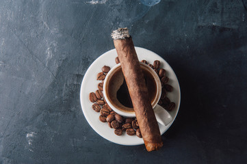 Cup of coffee, coffee beans, ashtray with cigar on dark background