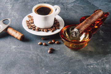 Cup of coffee, coffee beans, ashtray with cigar on dark background