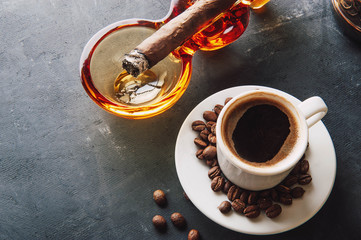 Cup of coffee, coffee beans, ashtray with cigar on dark background
