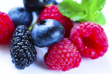 Close-up arrangement mixed, assorted berries including blackberries, strawberry, blueberry, raspberries and fresh leaf on white