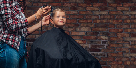 Cute preschooler boy getting haircut. Children hairdresser with trimmer is cutting little boy in a...