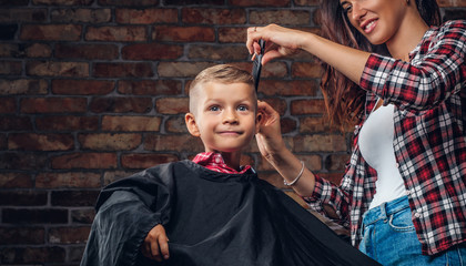 Smiling preschooler boy getting a haircut. Children hairdresser with scissors and comb is cutting...
