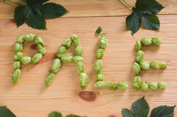 The inscription pale with hop cones on wooden background with leaves. Ingredient in beer industry....