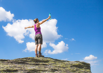 Junge Frau in Wanderschuhen steht auf Felsbrocken, blauer Himmel im Hintergrund