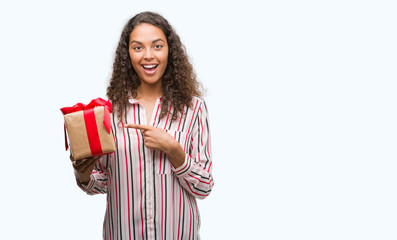 Young hispanic woman in love holding present very happy pointing with hand and finger