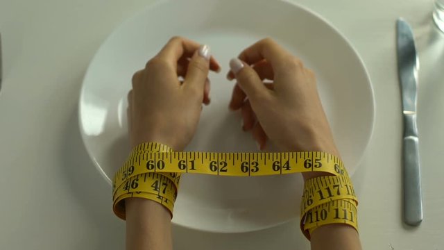 Hands tied with measuring tape lying on plate, obsession with diet, calories