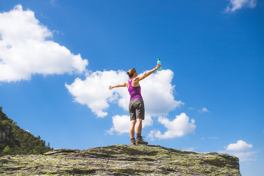 Junge Frau in Wanderschuhen steht auf Felsbrocken, blauer Himmel im Hintergrund