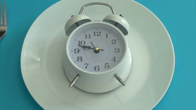 Alarm clock on empty plate, healthy diet schedule, daily nutrition, closeup