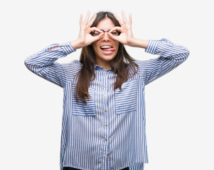 Young beautiful hispanic business woman doing ok gesture like binoculars sticking tongue out, eyes looking through fingers. Crazy expression.