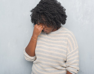 Young african american plus size woman over grey grunge wall wearing a sweater tired rubbing nose and eyes feeling fatigue and headache. Stress and frustration concept.