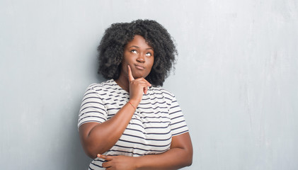 Young african american plus size woman over grey grunge wall with hand on chin thinking about question, pensive expression. Smiling with thoughtful face. Doubt concept.
