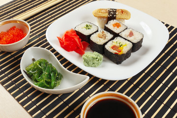 Sushi and makizushi with ginger and wasabi, hiyashi wakame salad, soy sauce and salmon caviar on a black bamboo makisu close up.